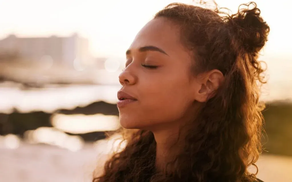 Young woman with curly hair breathing calmly with eyes closed in warm sunset light
