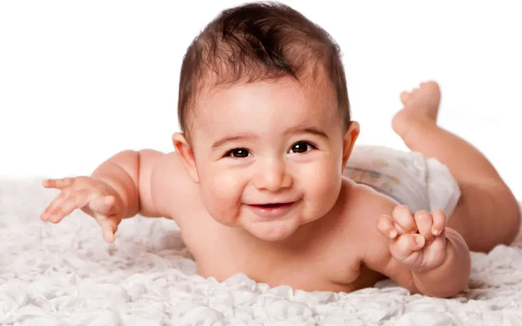 Smiling baby in a nappy lying on its front on a soft white blanket