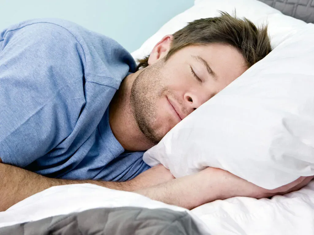 Man in a blue shirt sleeping peacefully on a white pillow