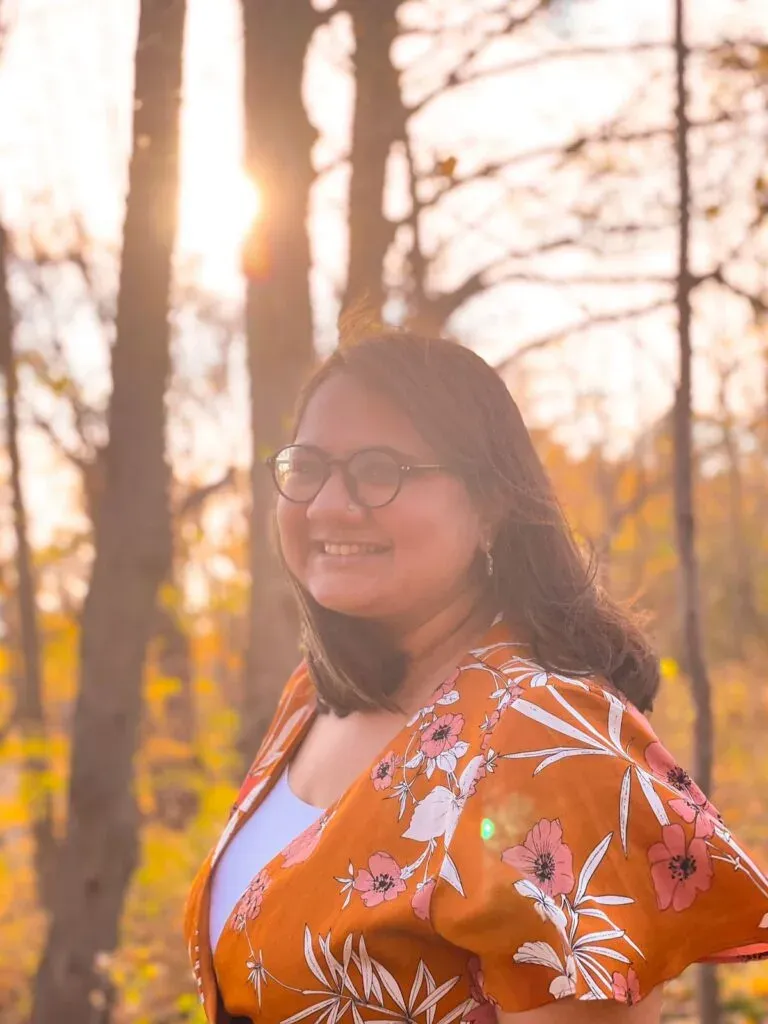 Smiling woman in an orange floral top standing in autumn woodland at sunset