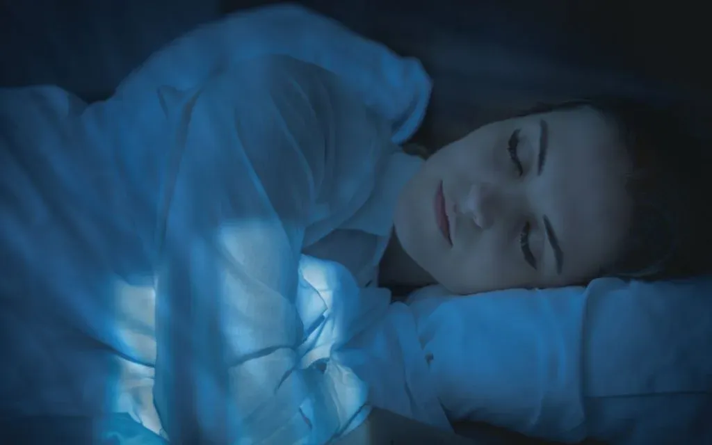 Woman asleep on her side under soft blue bedding in a darkened room