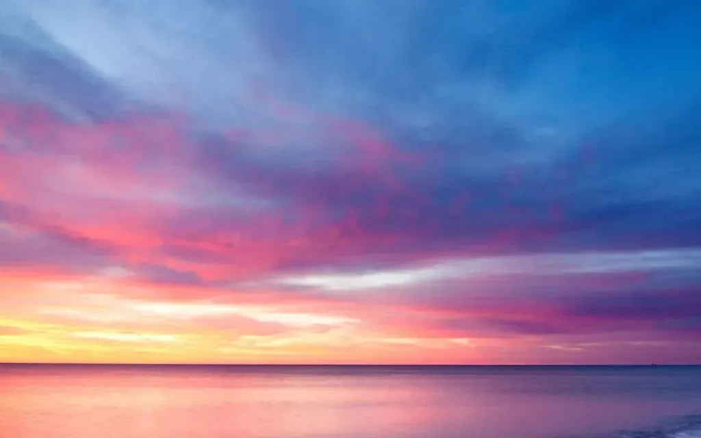 Pink and blue sunset sky over a calm sea, golden light glowing near the horizon