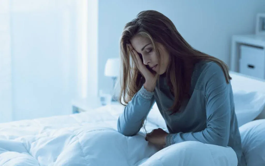 Tired woman in pyjamas sitting on the edge of a bed resting her head in her hand