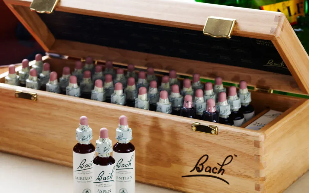 Wooden box holding rows of Bach flower remedy dropper bottles with three standing in front