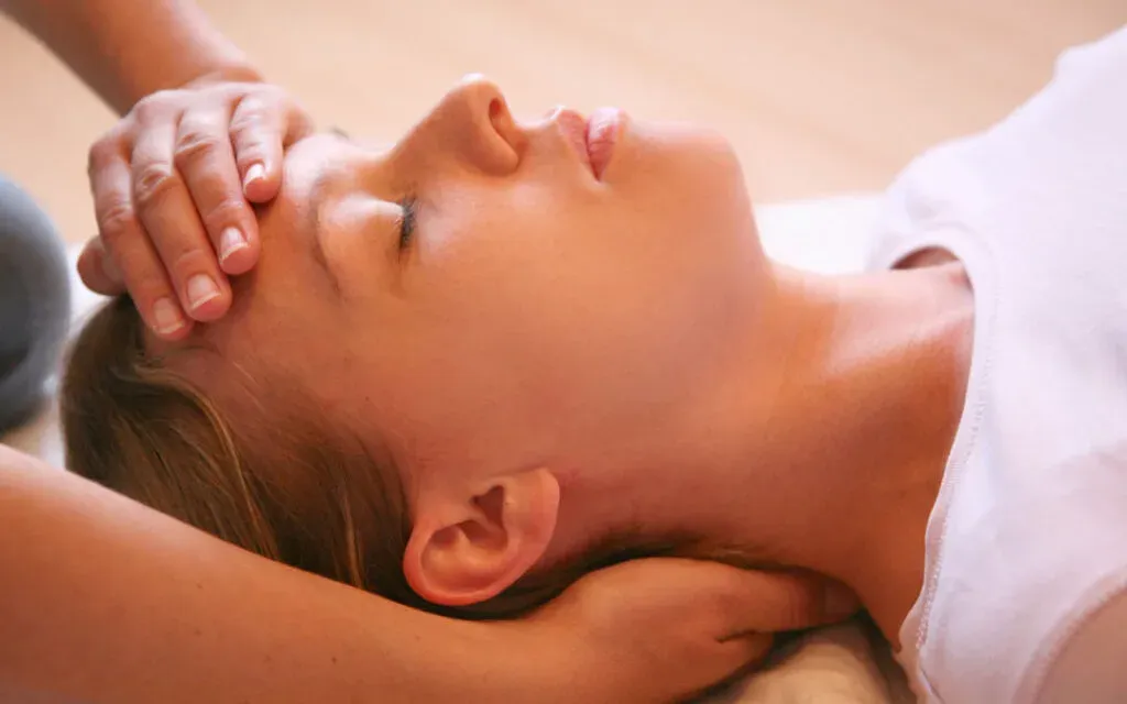 Woman lying with eyes closed as a therapist gently cradles her head during treatment