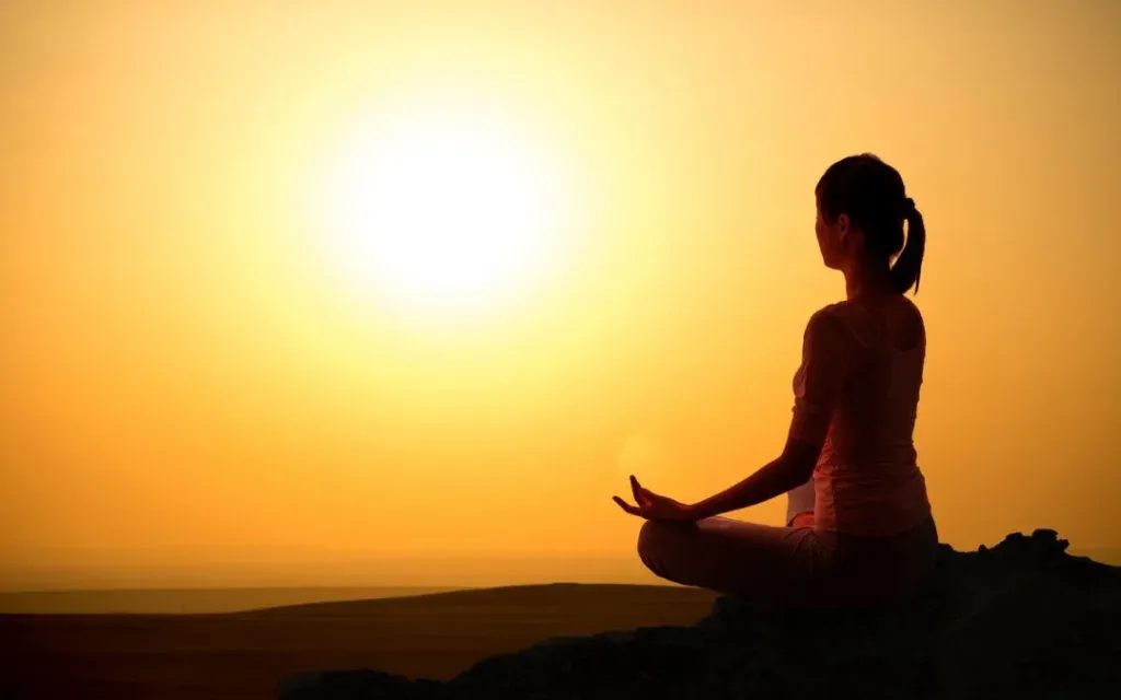 Silhouette of a woman sitting cross-legged in meditation against a golden sunset