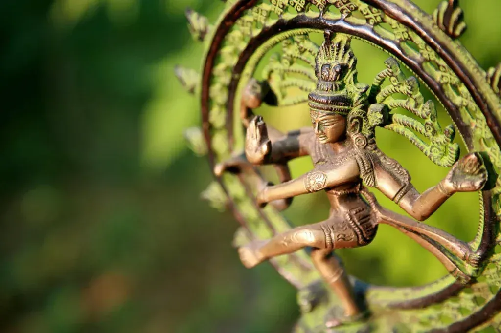 Brass statue of Lord Shiva as Nataraja dancing within a flaming arch, greenery blurred behind