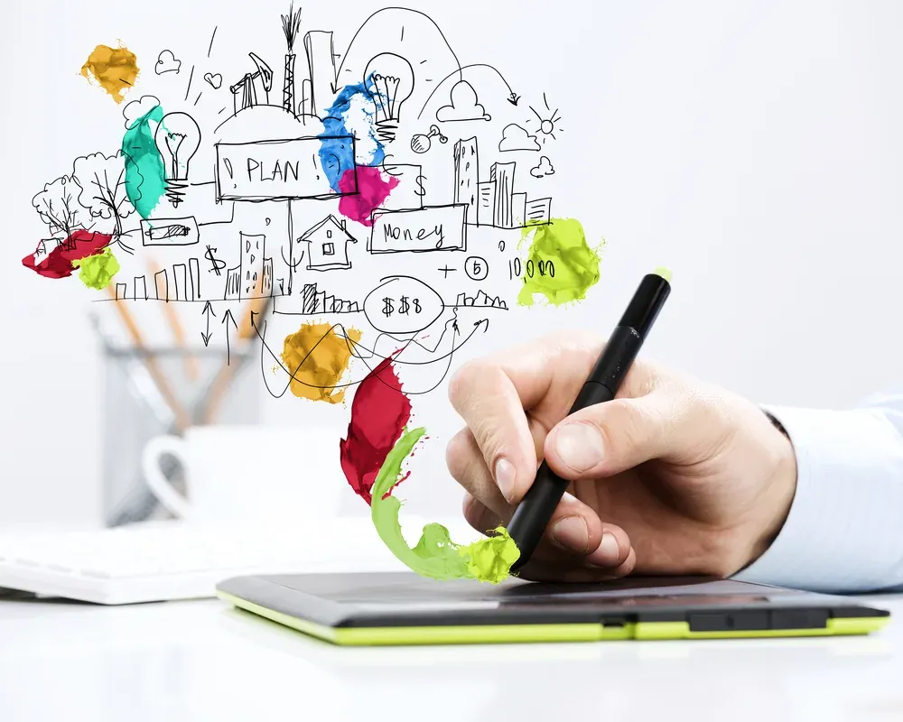 Hand holding a pen over a tablet beneath colourful doodles of plans, money and ideas