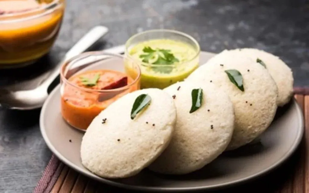 Plate of steamed idlis served with red and green chutneys and sambar