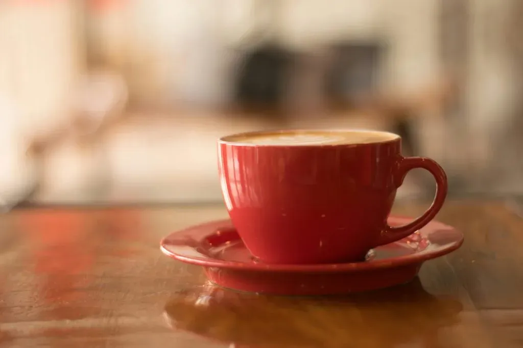 Red cup of coffee on a matching saucer resting on a polished wooden table