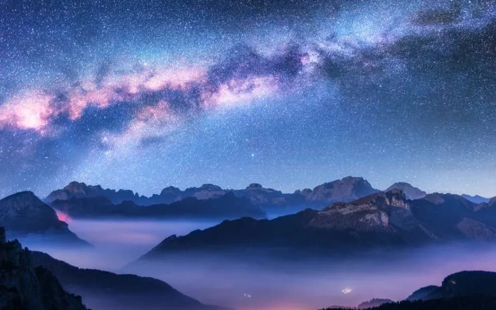The Milky Way arching over misty mountain peaks under a star filled night sky