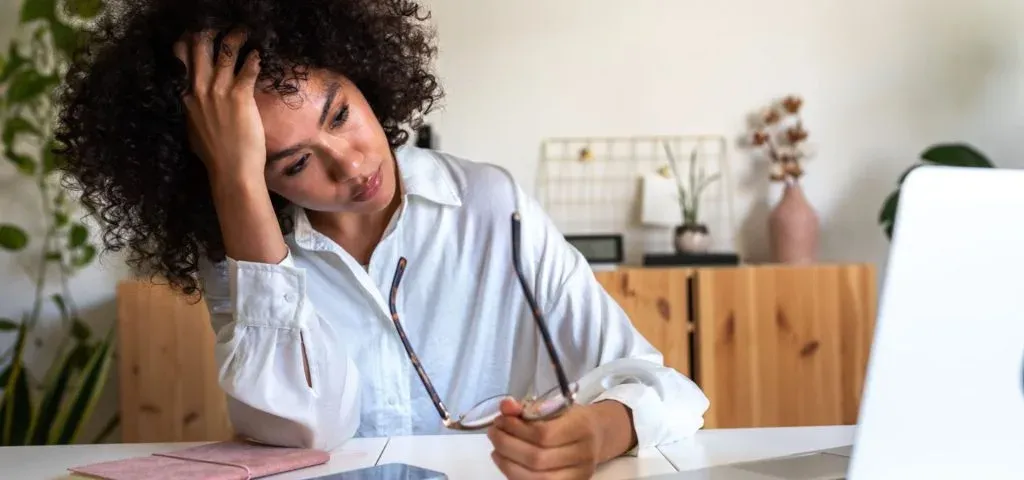 Tired woman resting her head on her hand at a desk, holding her glasses