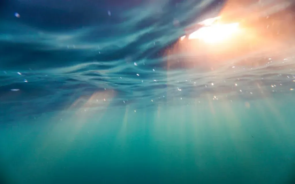 Underwater view of sunlight streaming through the rippling surface of blue green sea