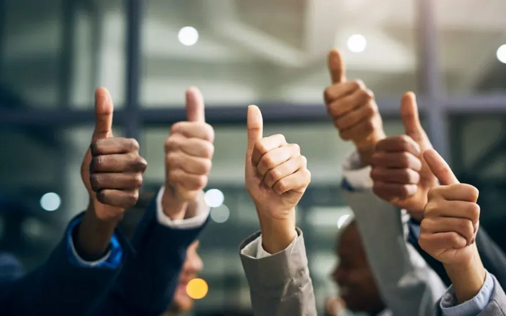 Several people in suits raising their hands together in a thumbs-up gesture