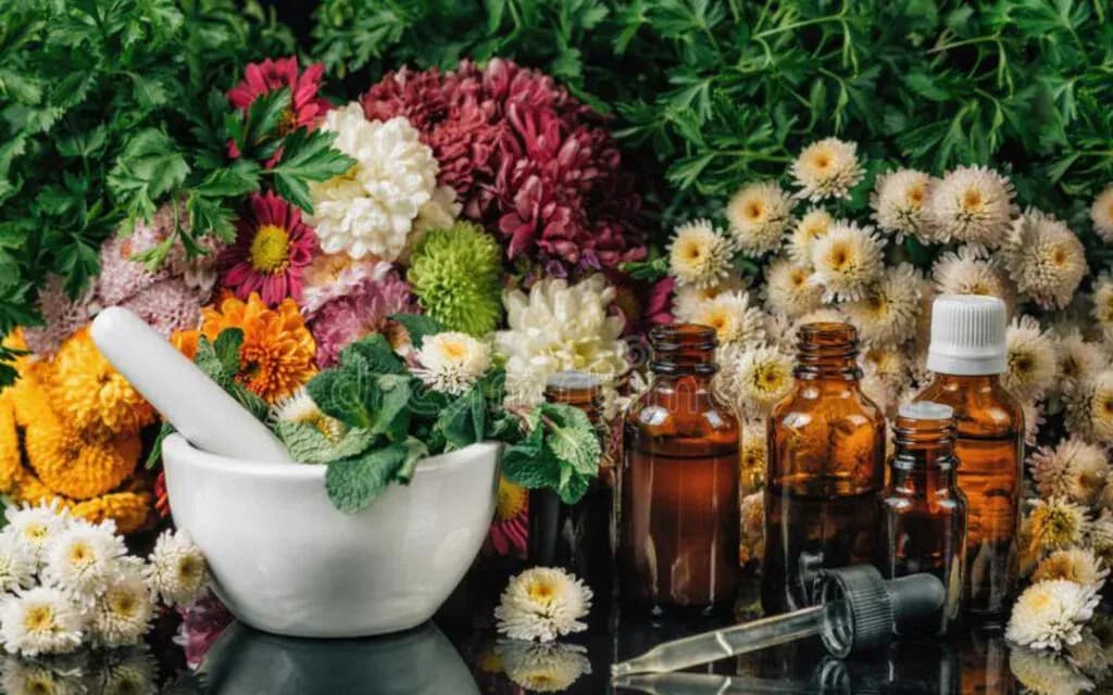 White mortar of fresh mint beside amber remedy bottles and a dropper, surrounded by flowers