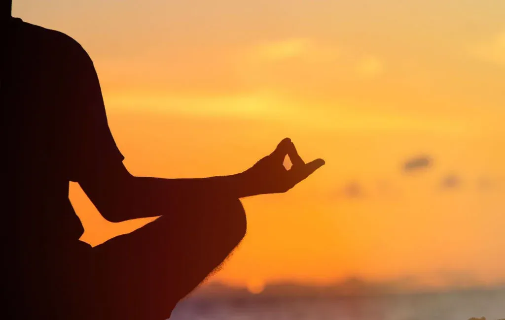 Silhouette of a person sitting cross legged in meditation against an orange sunset sky