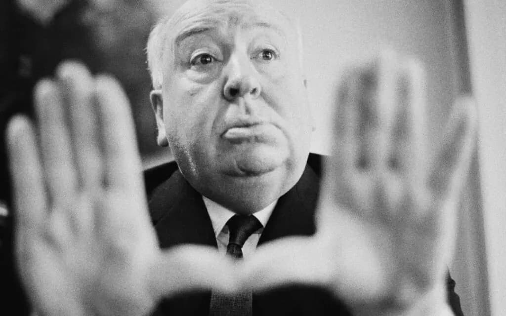 Black and white portrait of Alfred Hitchcock framing his face with his raised hands