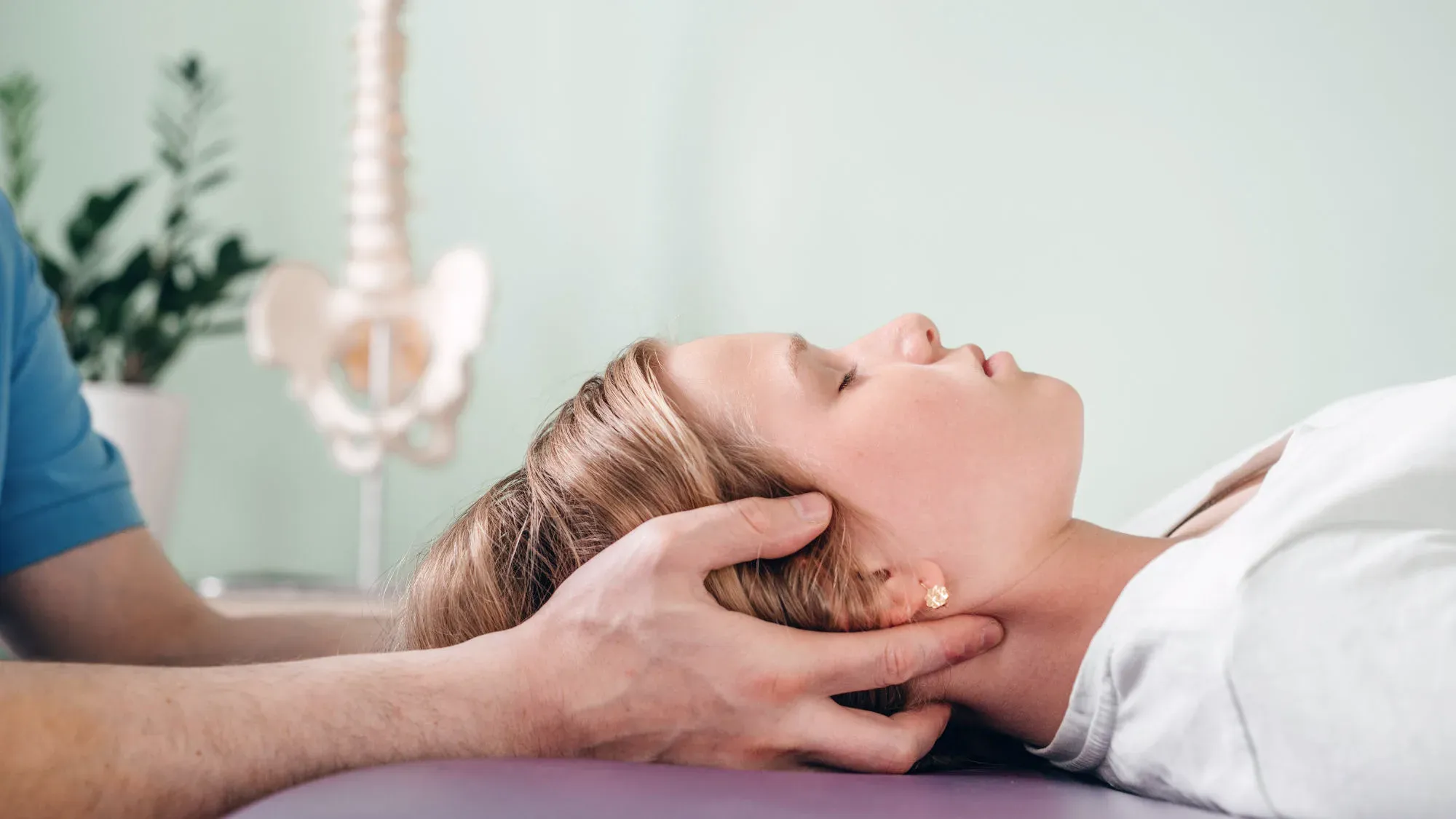 A therapist cradling a woman's head and neck as she lies on a treatment couch