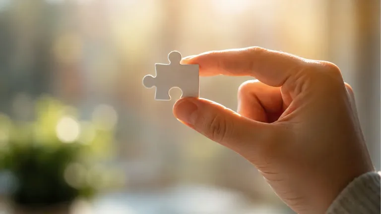 A hand holding a single jigsaw piece up to the light