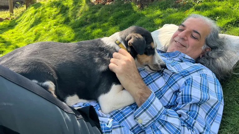 Khurshed lying on the grass with a black and white dog curled against him