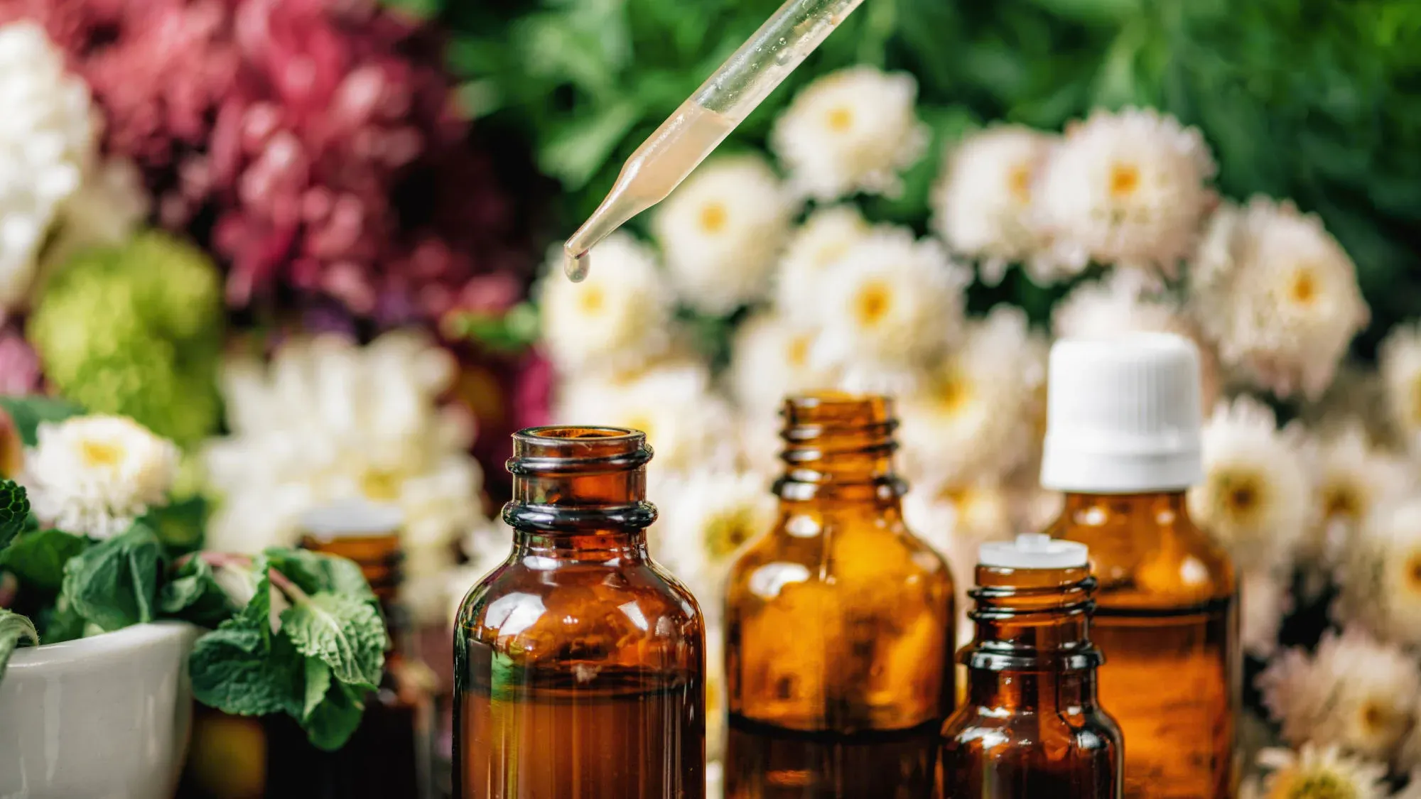 Amber dropper bottles among flowers, with a pipette above one of them