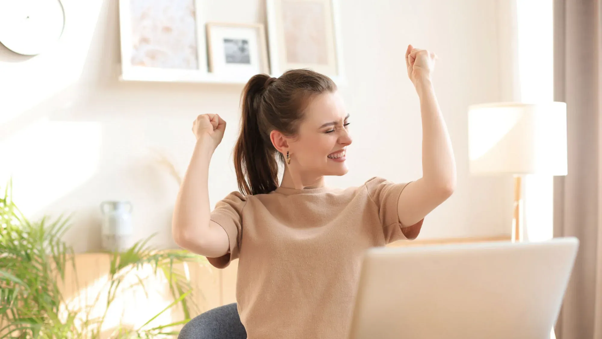 A woman at a laptop with both fists raised in delight