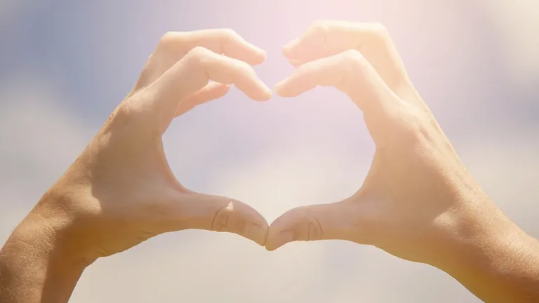 Two hands held together to make the shape of a heart against a soft sky