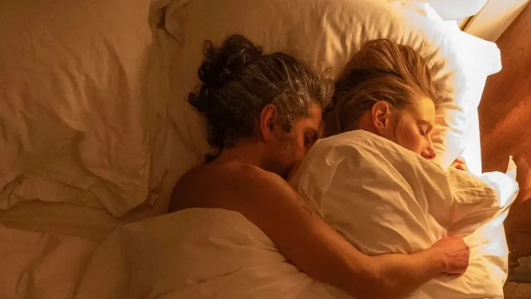 A couple asleep together under white bedding in warm lamplight