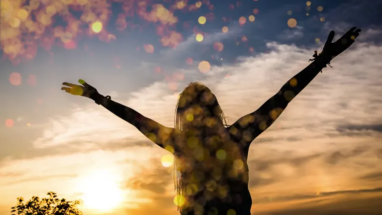 A woman standing with her arms raised against a sunset sky