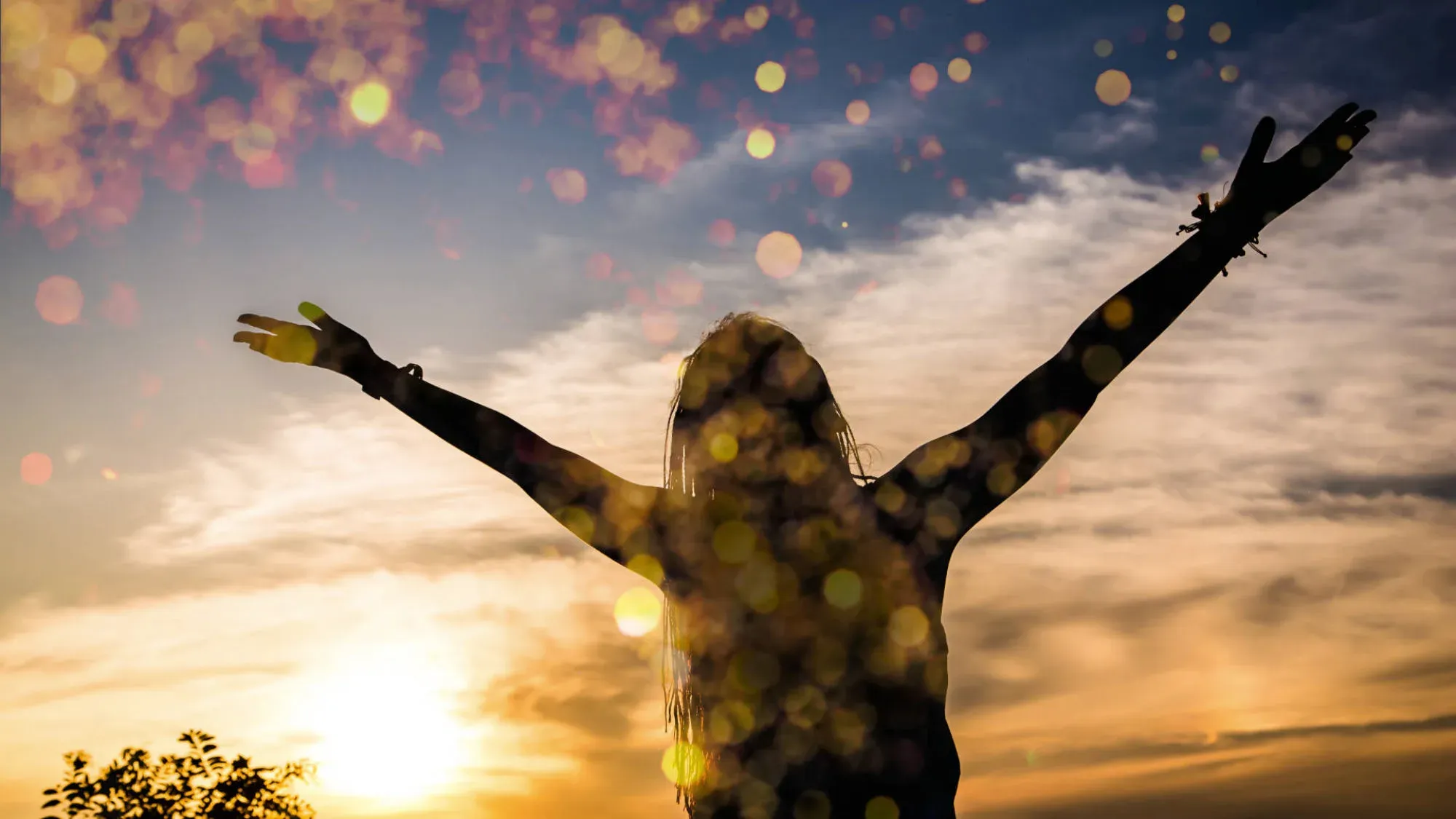 A woman standing with her arms raised against a sunset sky