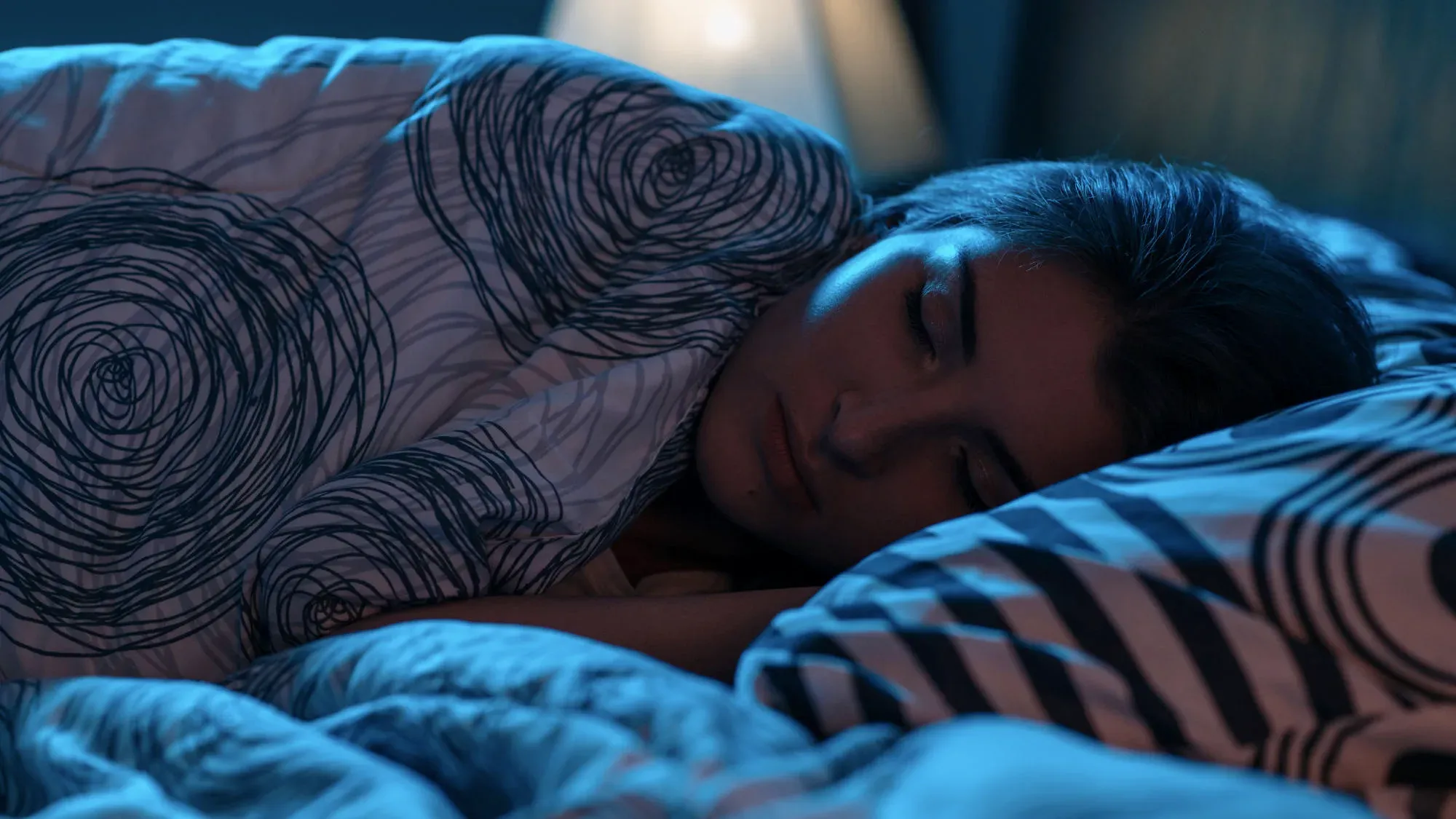 A woman asleep under a patterned quilt in blue light