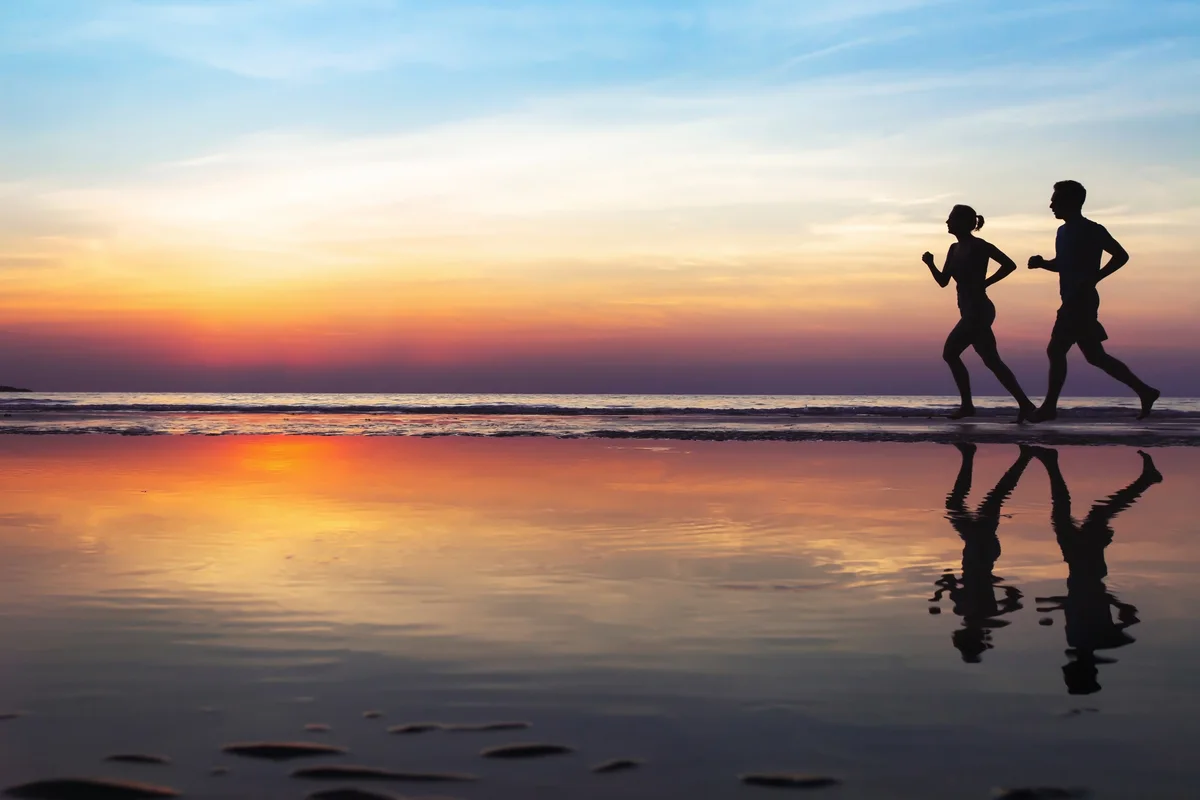 Two people jogging on a beach at sunset